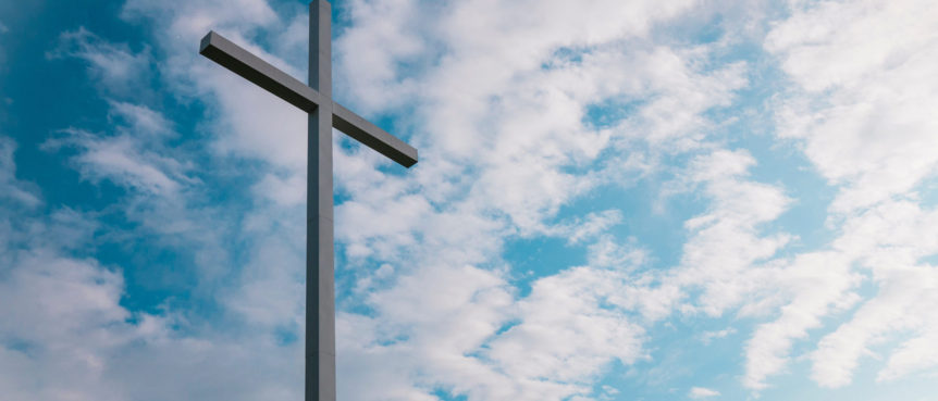 A cross is shown against the sky with clouds.