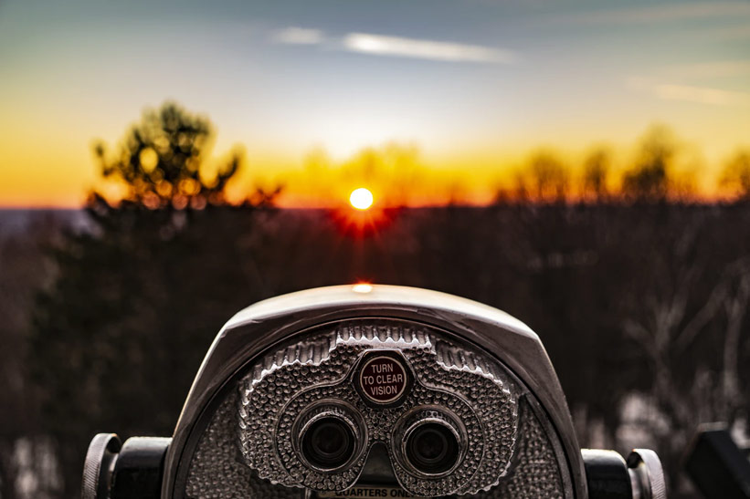 A coin operated telescope with the sun setting in the background.